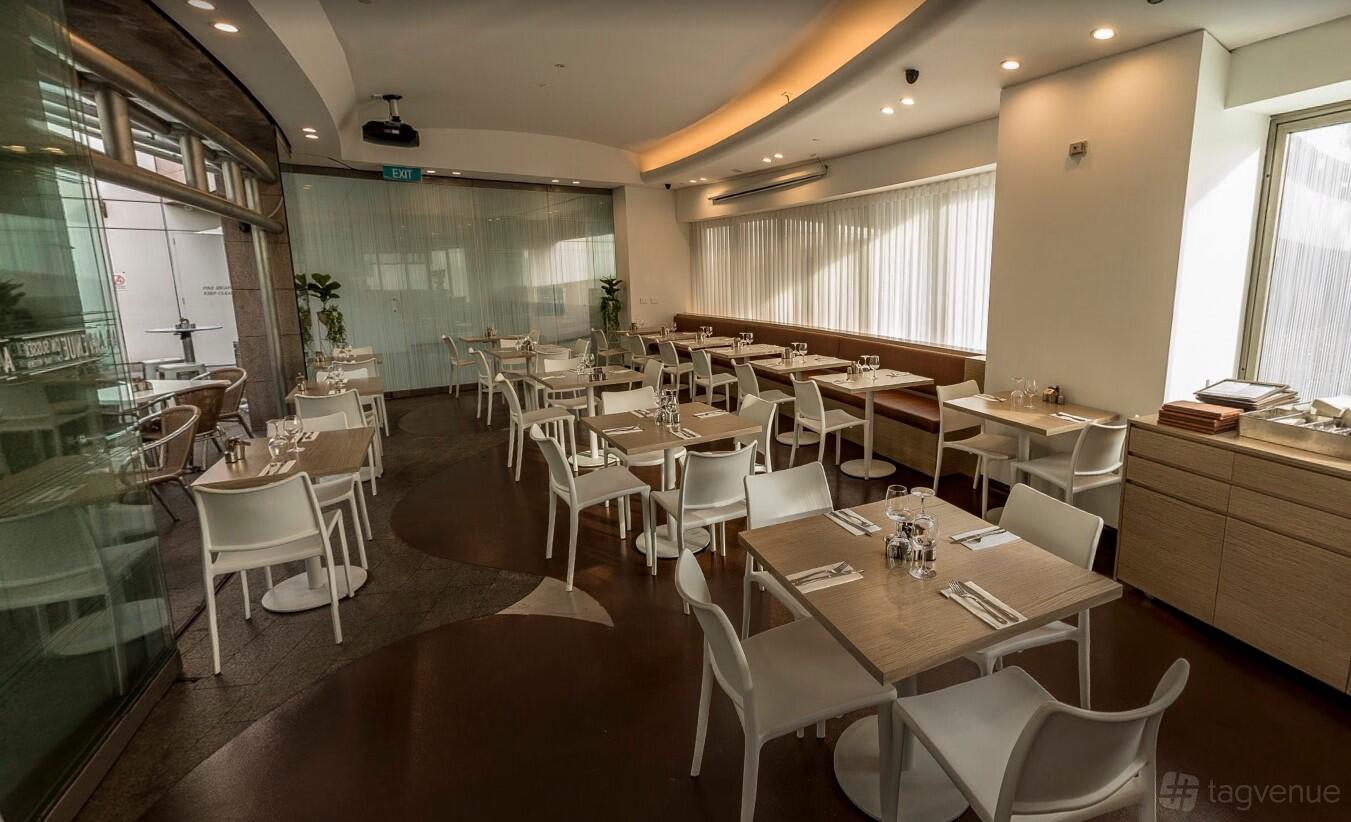 A dining room in a cafe with floor-to-ceiling windows, light wood tables, and white chairs at Avenue On Sussex.