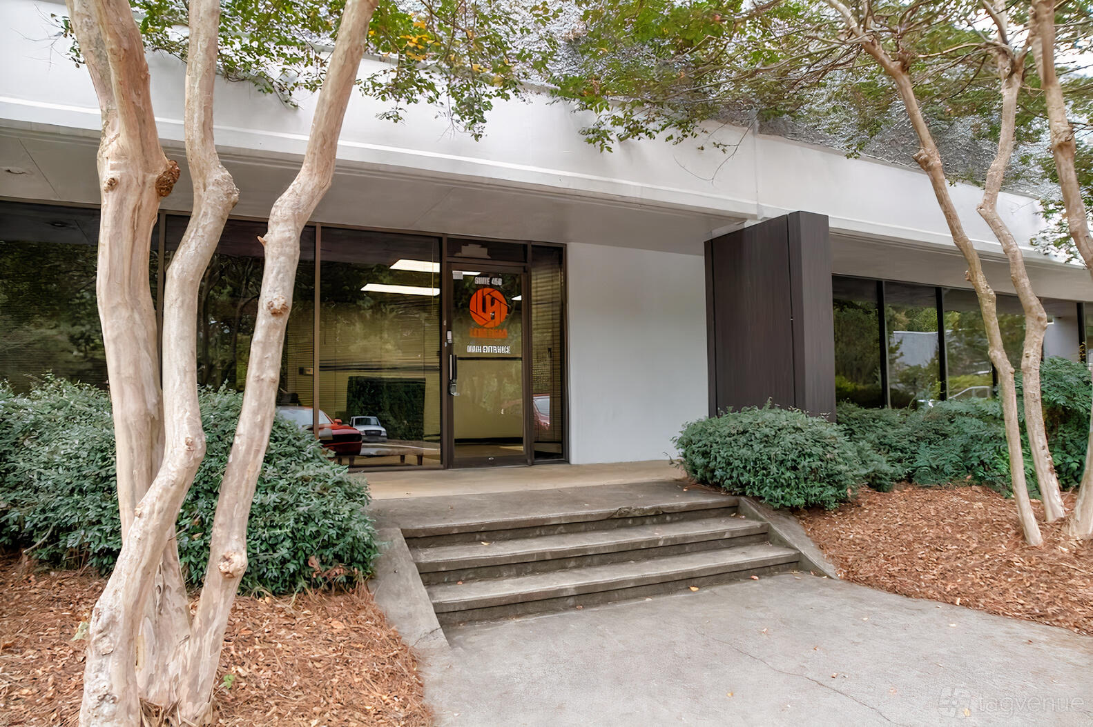 A film and photo studio with glass entry doors, large windows, and landscaped trees at Lens Head Studios.