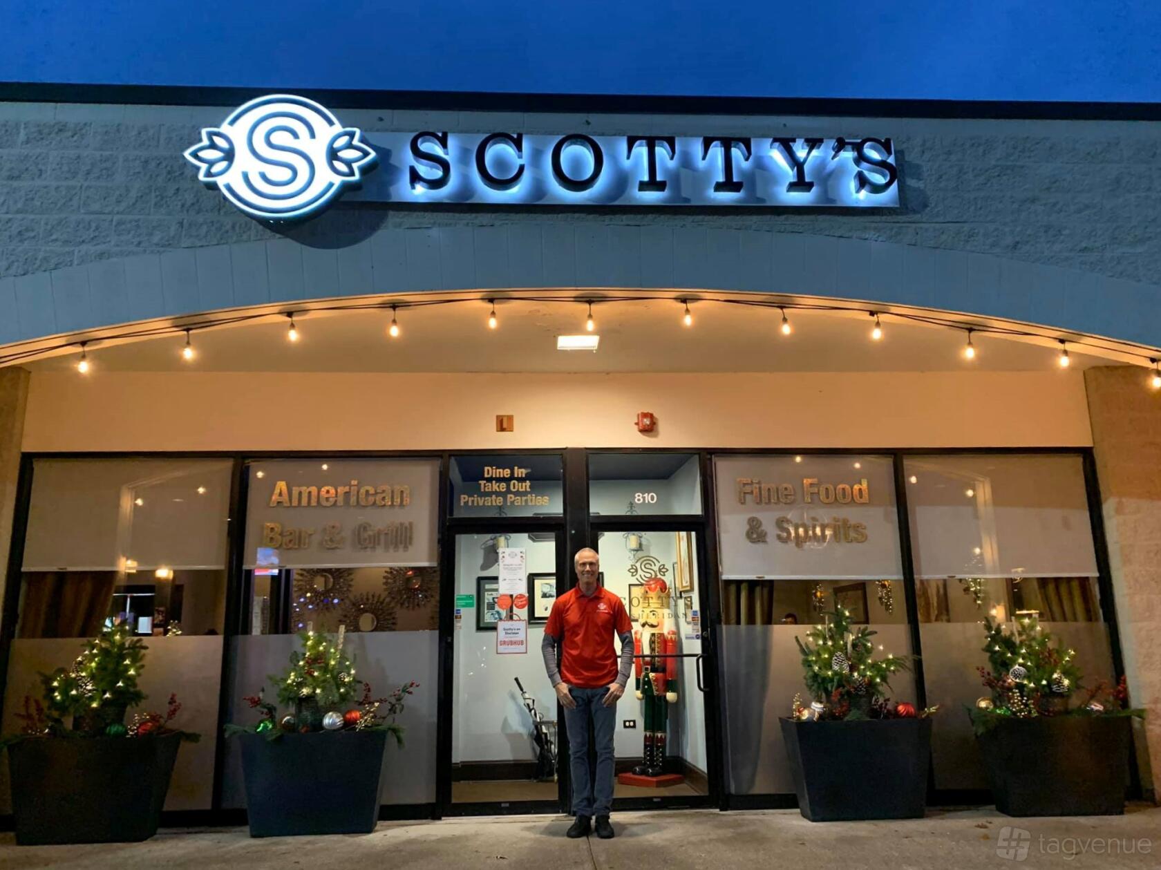 A restaurant entrance with illuminated signage, festive planters, and string lights at Scotty's on Sheridan.