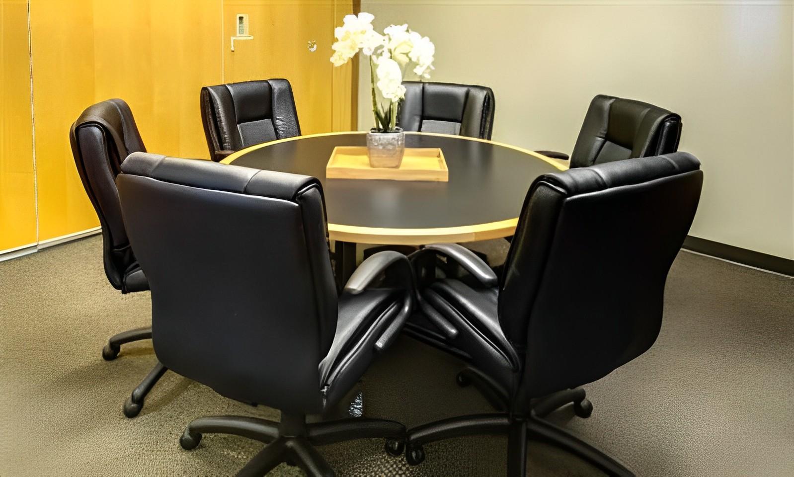 A meeting room with a round table, black leather office chairs, and a potted orchid centerpiece at Intelligent Office in Rockville, MD.