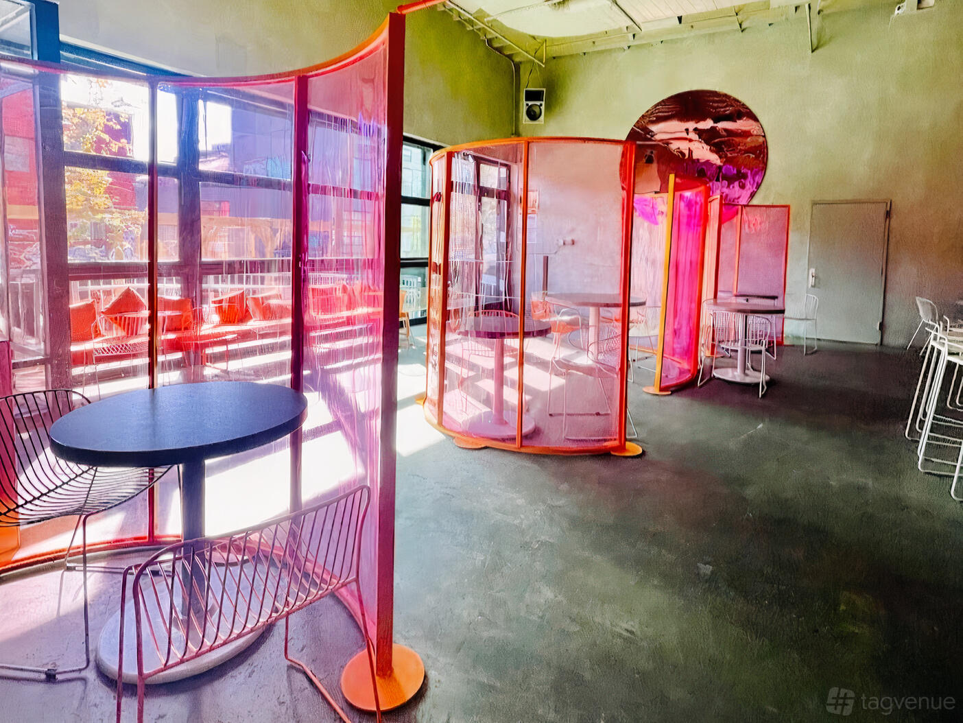 An event space with pink transparent partitions, wire chairs, and floor-to-ceiling windows at Wandering Barman.