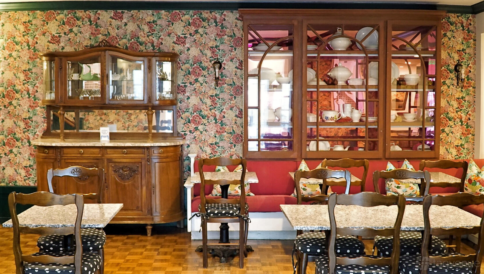 An event space with floral wallpaper, wooden dining tables, vintage china cabinets, and patterned chairs at White Swan Inn.