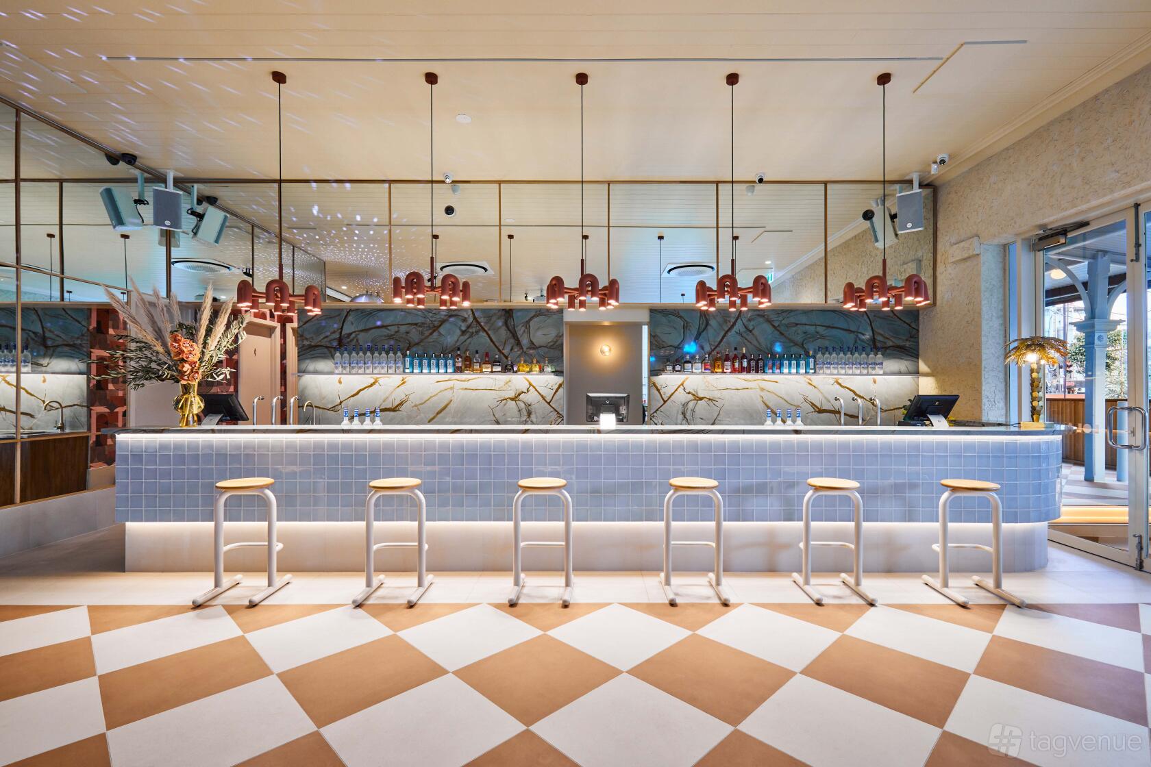 An event space with a marble-topped bar, modern pendant lights, and checkered flooring at LOLA St Kilda.
