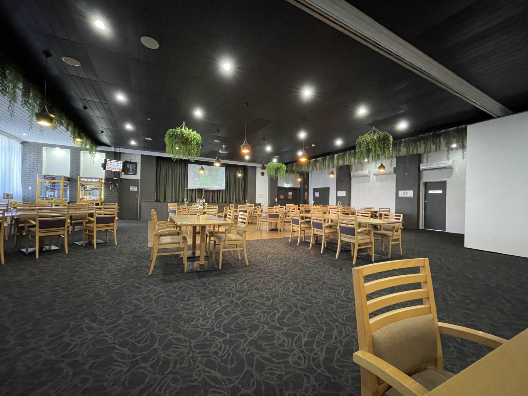 An auditorium with round wooden tables, chairs, hanging greenery, and stage at Berowra RSL Club.