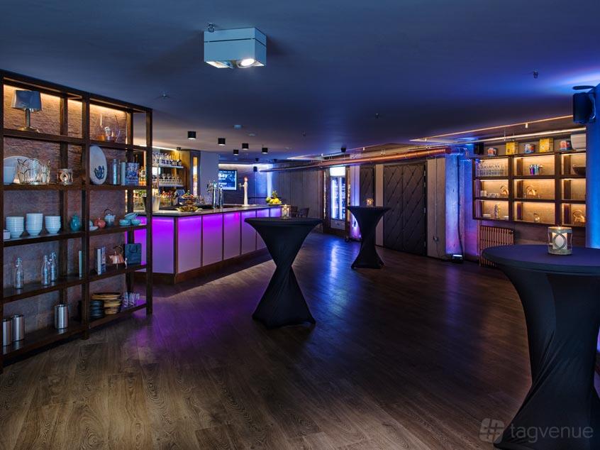 An event space with a backlit bar, high-top cocktail tables, and wooden shelving at Medley.