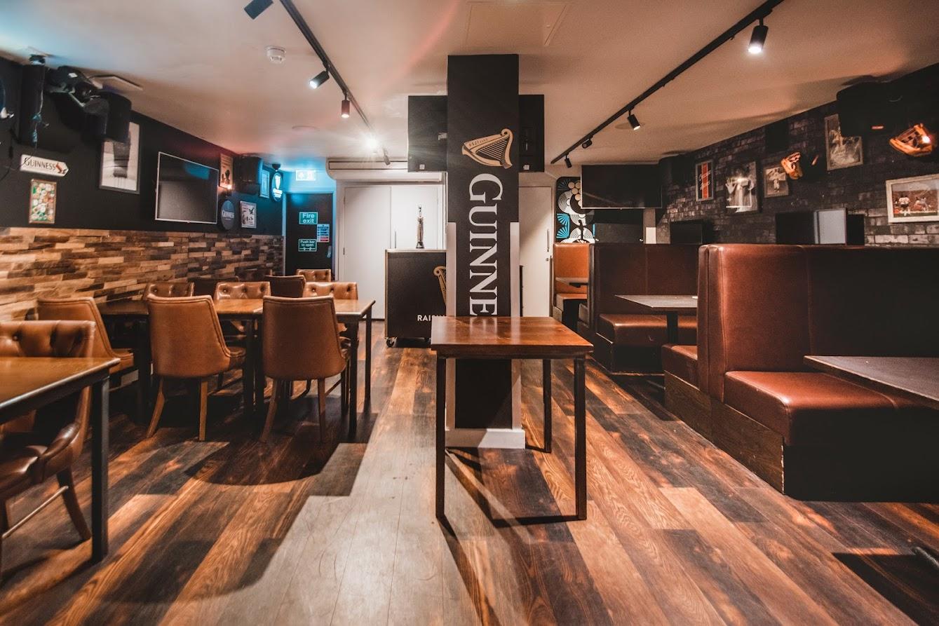 An event space in a bar with leather booths, wooden tables, and Guinness signage at Belushi's & The Dugout London Bridge.
