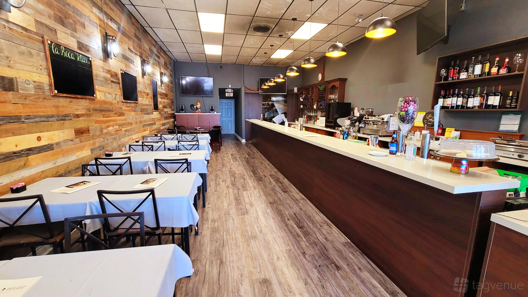 A restaurant with wood-paneled walls, pendant lighting, and white tablecloths at La Boca Felizz - Taapas & Grill.