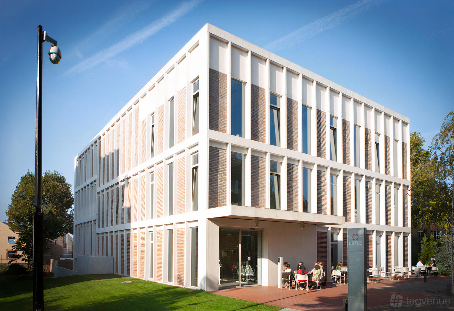 A conference centre with a modern glass entrance, brick façade, and outdoor seating area at ORTUS Conference and Events Venue.