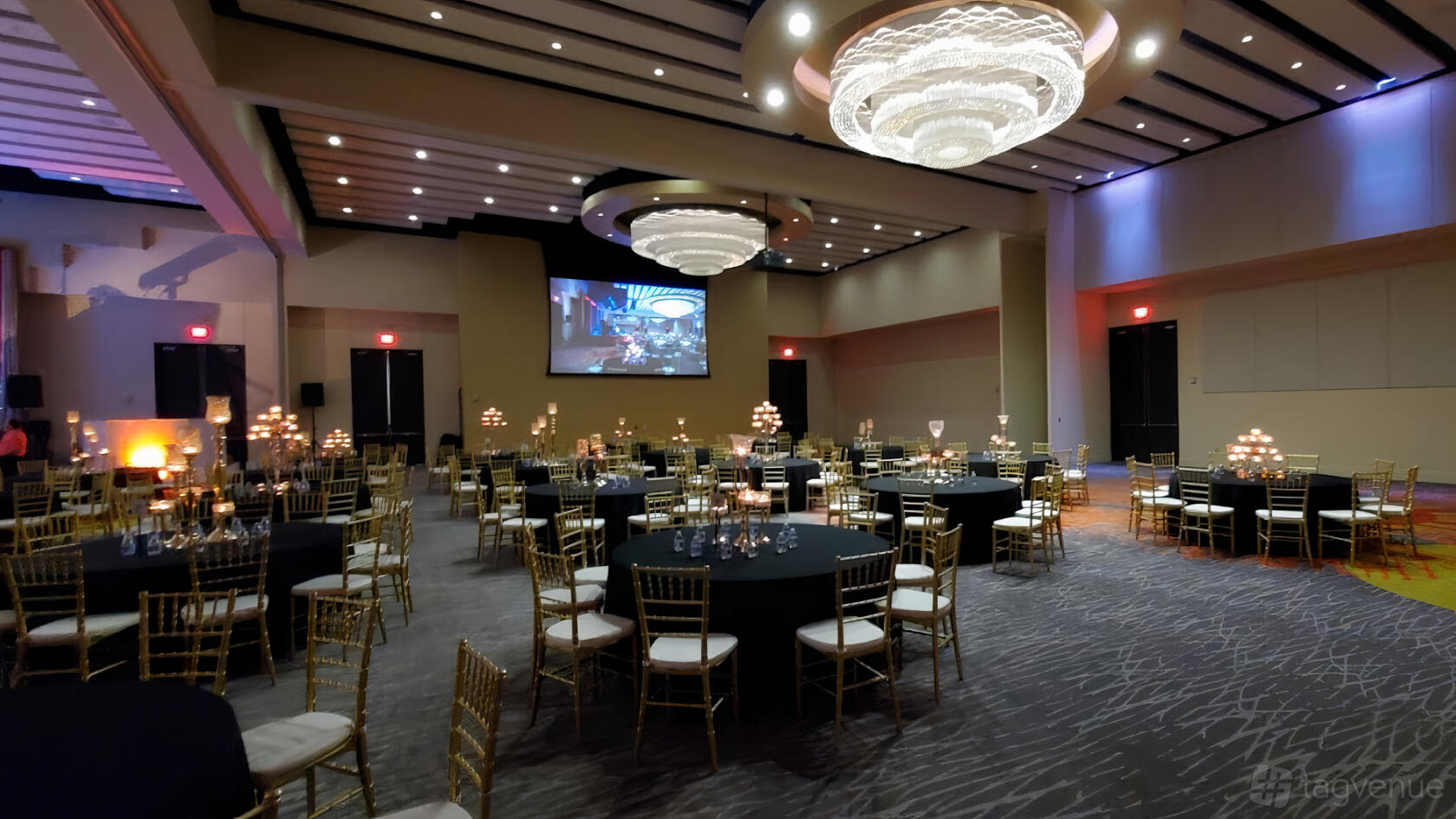 An event venue with round tables, gold chairs, candle centerpieces, and large chandeliers at SLPS Event Center.