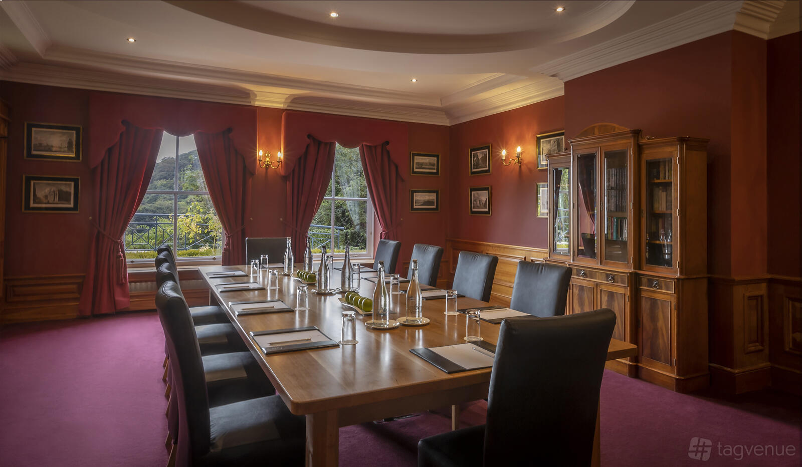 A hotel meeting room with a long wooden table, high-backed chairs, red walls, and large windows at Glenview Hotel & Leisure Club.