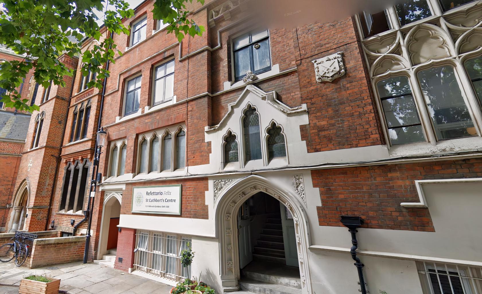 A brick hall with arched windows, detailed stonework, and a grand entrance at Refettorio Felix at St Cuthbert's.