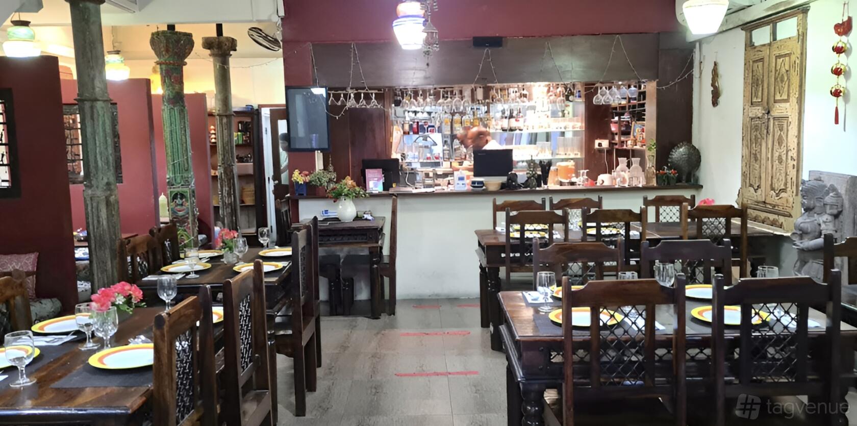 A restaurant with dark wooden tables set with plates and wine glasses facing an open bar at Kinara - East Coast.