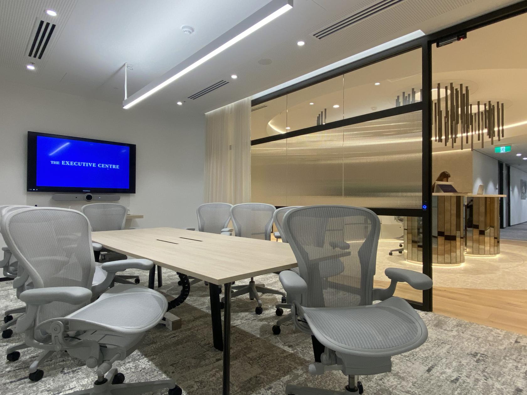 A meeting room with ergonomic chairs, a large screen, and a wooden conference table at Angel Place.