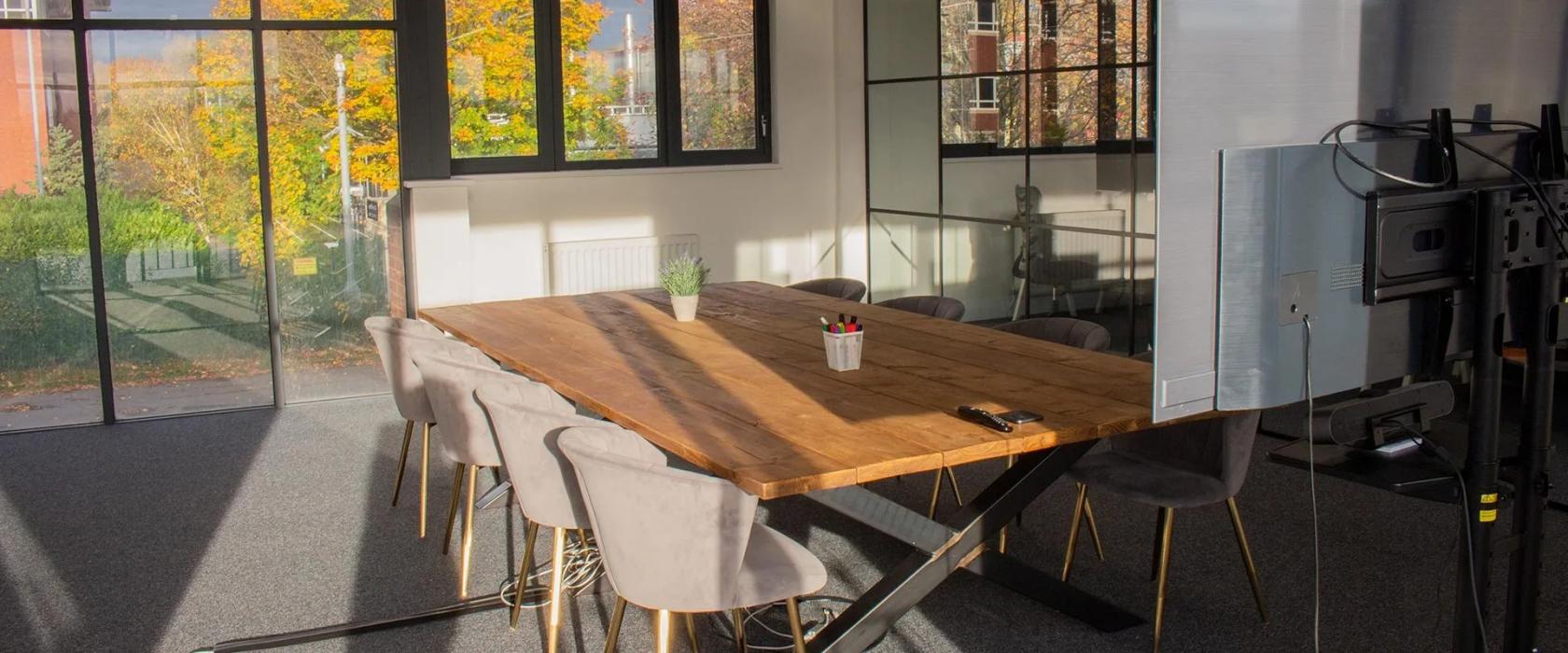 A boardroom with a large wooden table, velvet chairs, and natural light from floor-to-ceiling windows at Kingfisher Studios.