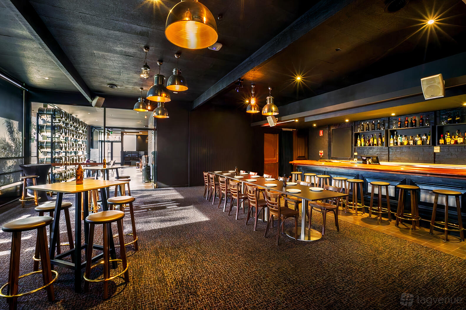 A pub with high tables, wooden stools, and pendant lighting next to a long bar at The Cheeky Squire.