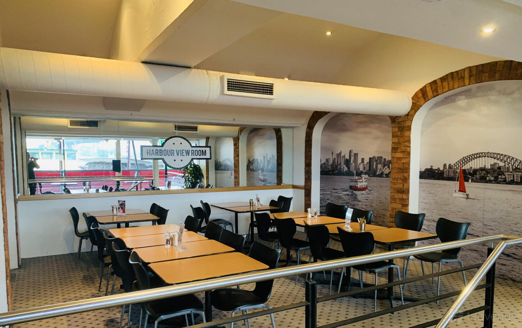 An event space in a restaurant with harbor-themed wall murals, rectangular tables, and black chairs at City Extra.