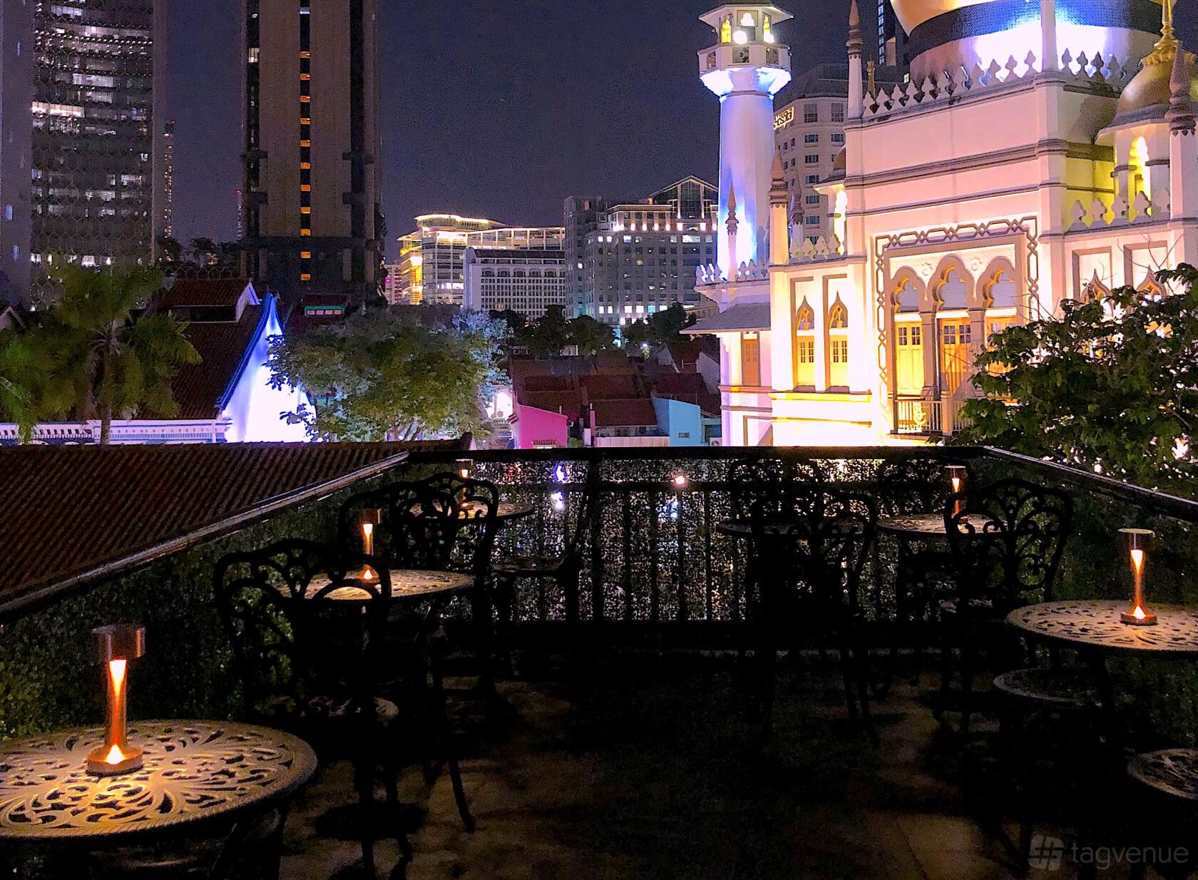 An outdoor restaurant terrace with ornate metal tables and candlelit seating overlooking city lights at Maison Ikkoku.