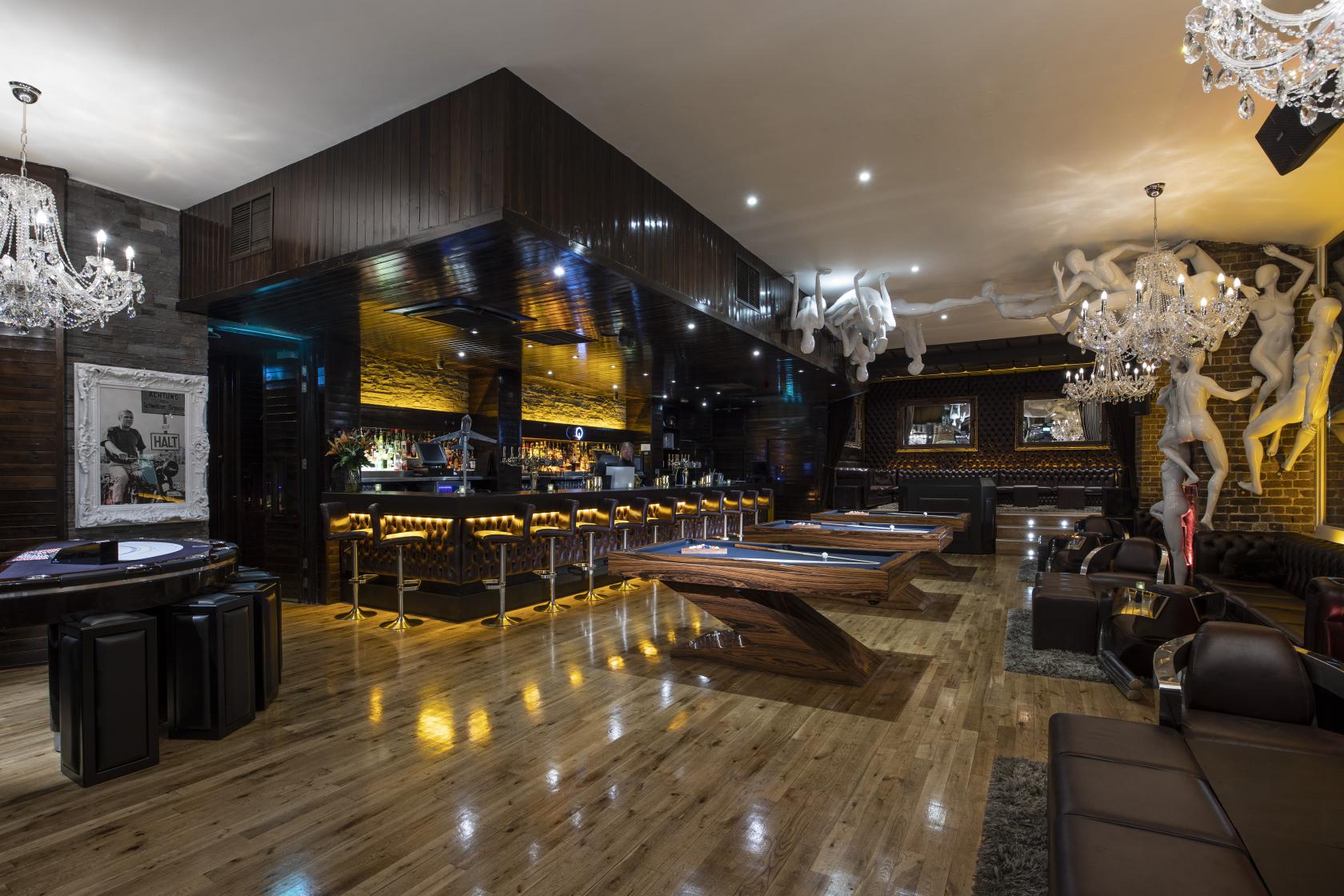 An event space in a bar with polished wood floors, chandeliers, pool tables, and a backlit bar at Q Shoreditch.