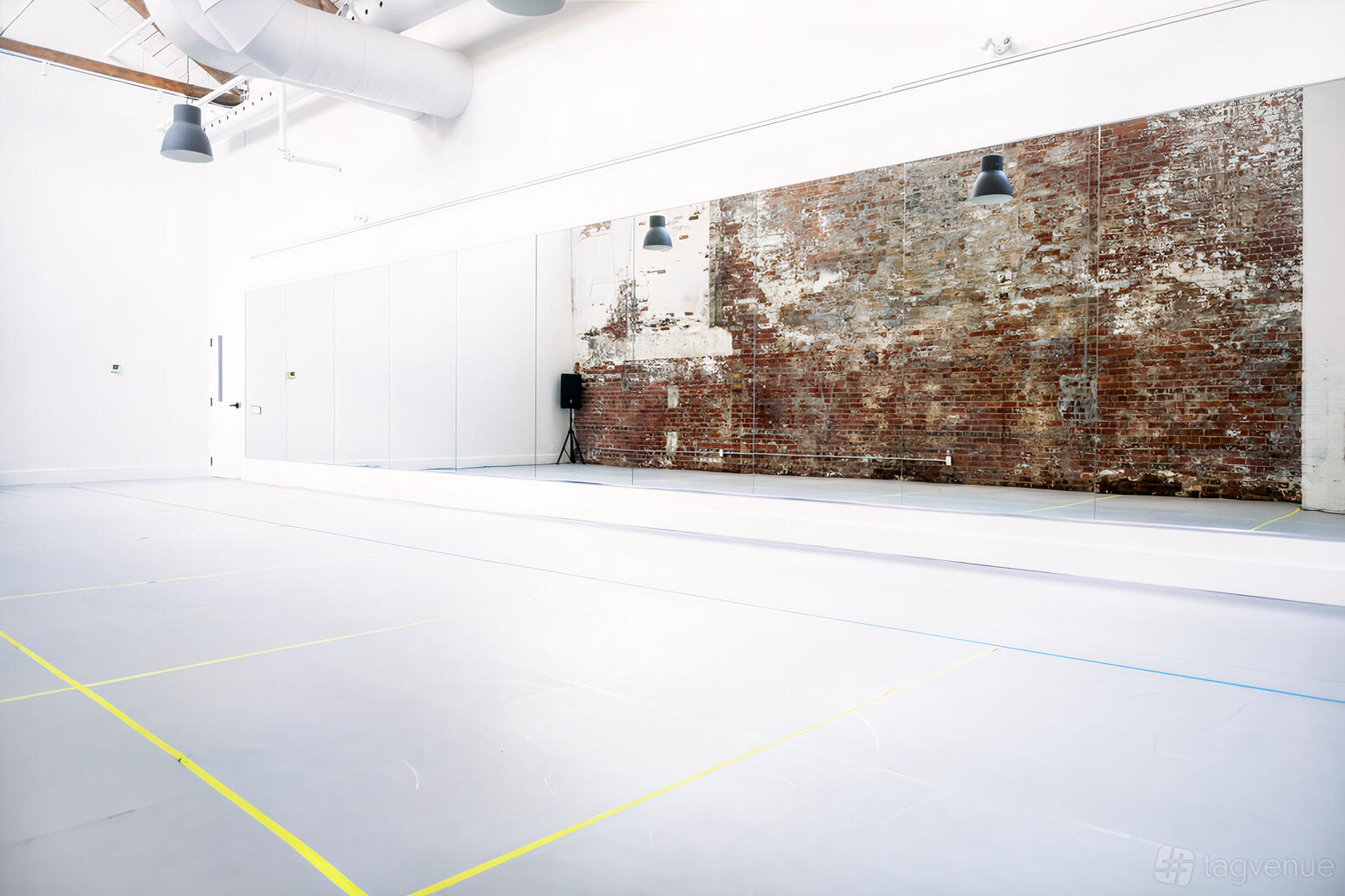 A rehearsal studio with a full-length wall mirror, exposed brick wall, and white flooring at City Dance Corps.