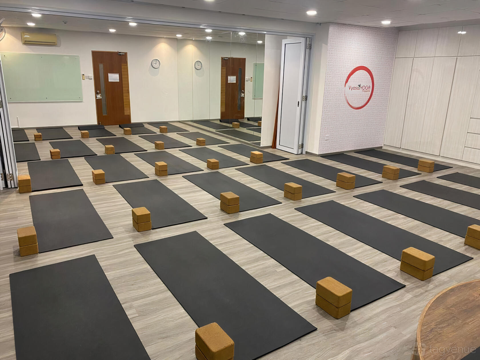 A yoga studio with black mats and cork yoga blocks arranged on light wood flooring at Vyasa Yoga Singapore.