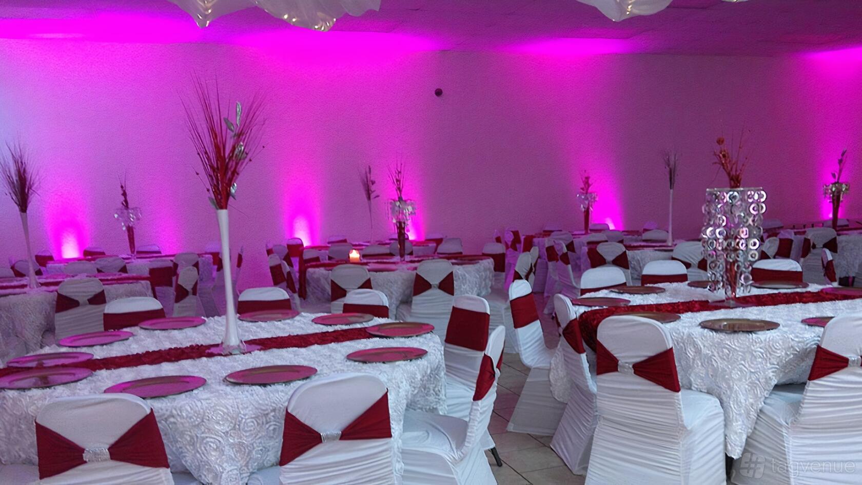 A ballroom with round tables draped in white linens, red chair sashes, and pink uplighting at Star Banquet and Event Center, LLC.