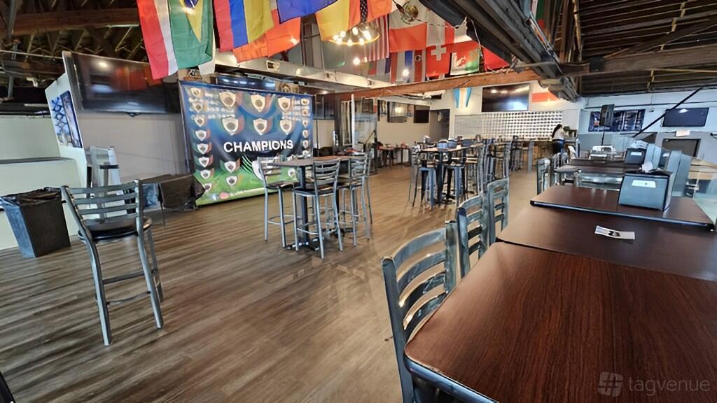 An indoor stadium lounge with multiple tables, chairs, flags, and a large 'Champions' backdrop at Chicago Futsal Academy.