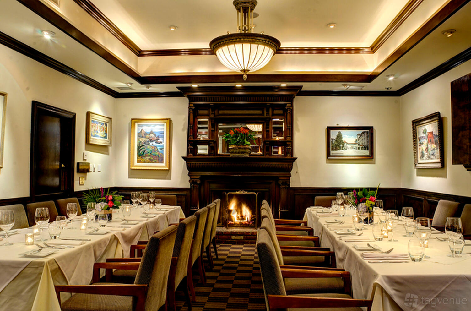 A restaurant dining room with a fireplace, chandelier lighting, artwork, and tables set with glassware at Parkway Grill.