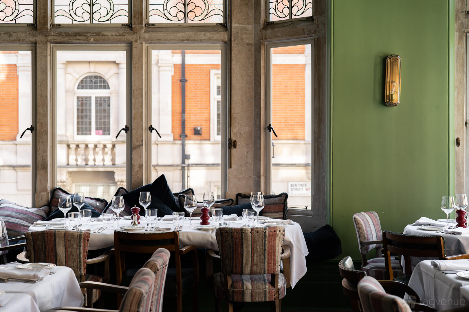 A dining room in a pub with large windows, striped upholstered chairs, and tables set with white linens at The Coach Makers Arms Pub Marylebone.