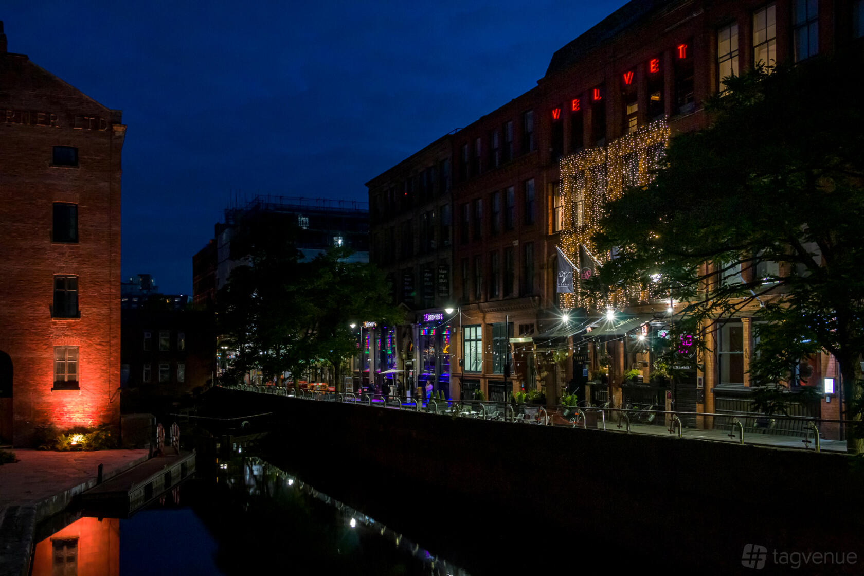 A hotel with illuminated exterior lights, riverside seating, and visible signage at Velvet Hotel, Bar & Brasserie.