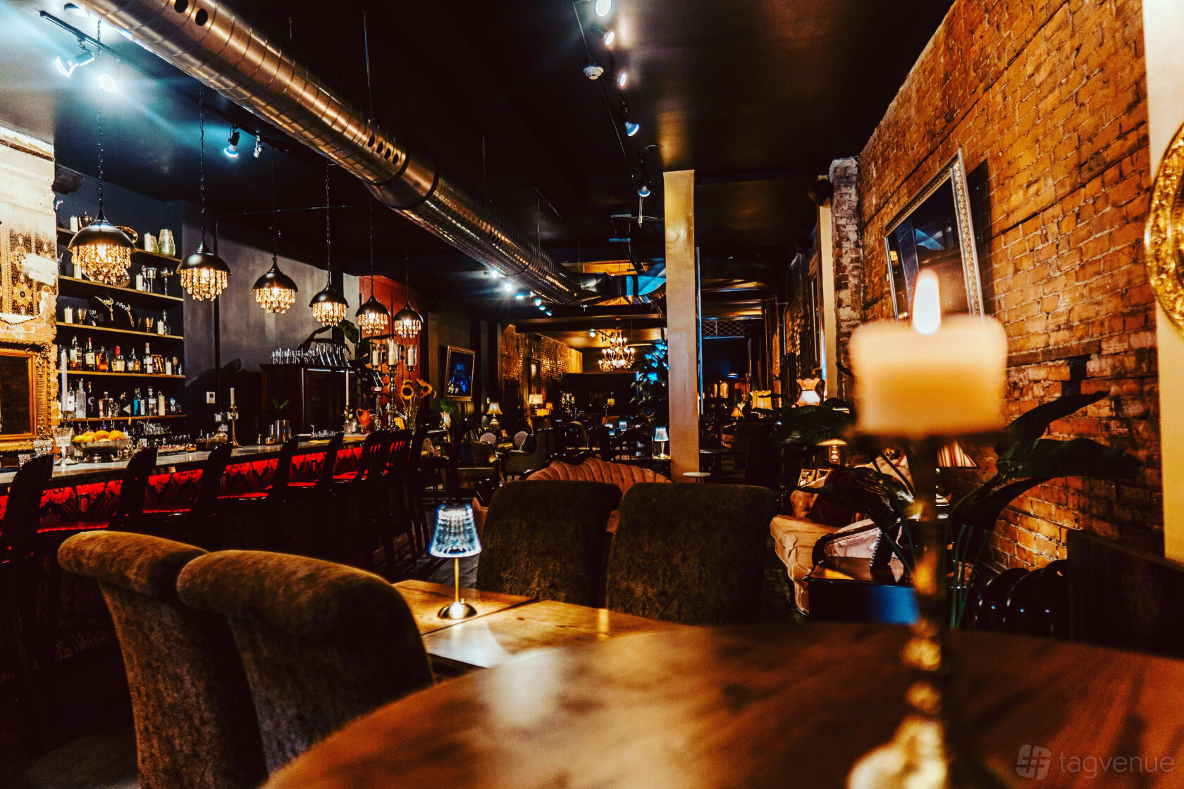 A bar with exposed brick walls, chandeliers, and cozy seating areas at MY HOUSE Lounge & Events.