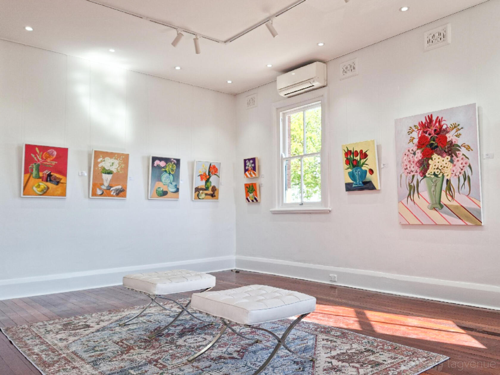 A gallery with hardwood floors, white walls, colorful artwork, and tufted benches at SOHOStudio.