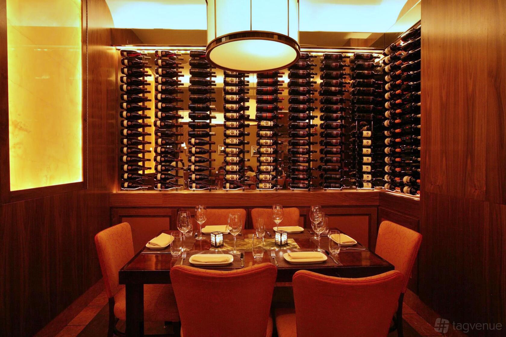 An intimate event space with a wall of wine bottles, wooden accents, and orange upholstered chairs at Pera Mediterranean Brasserie.