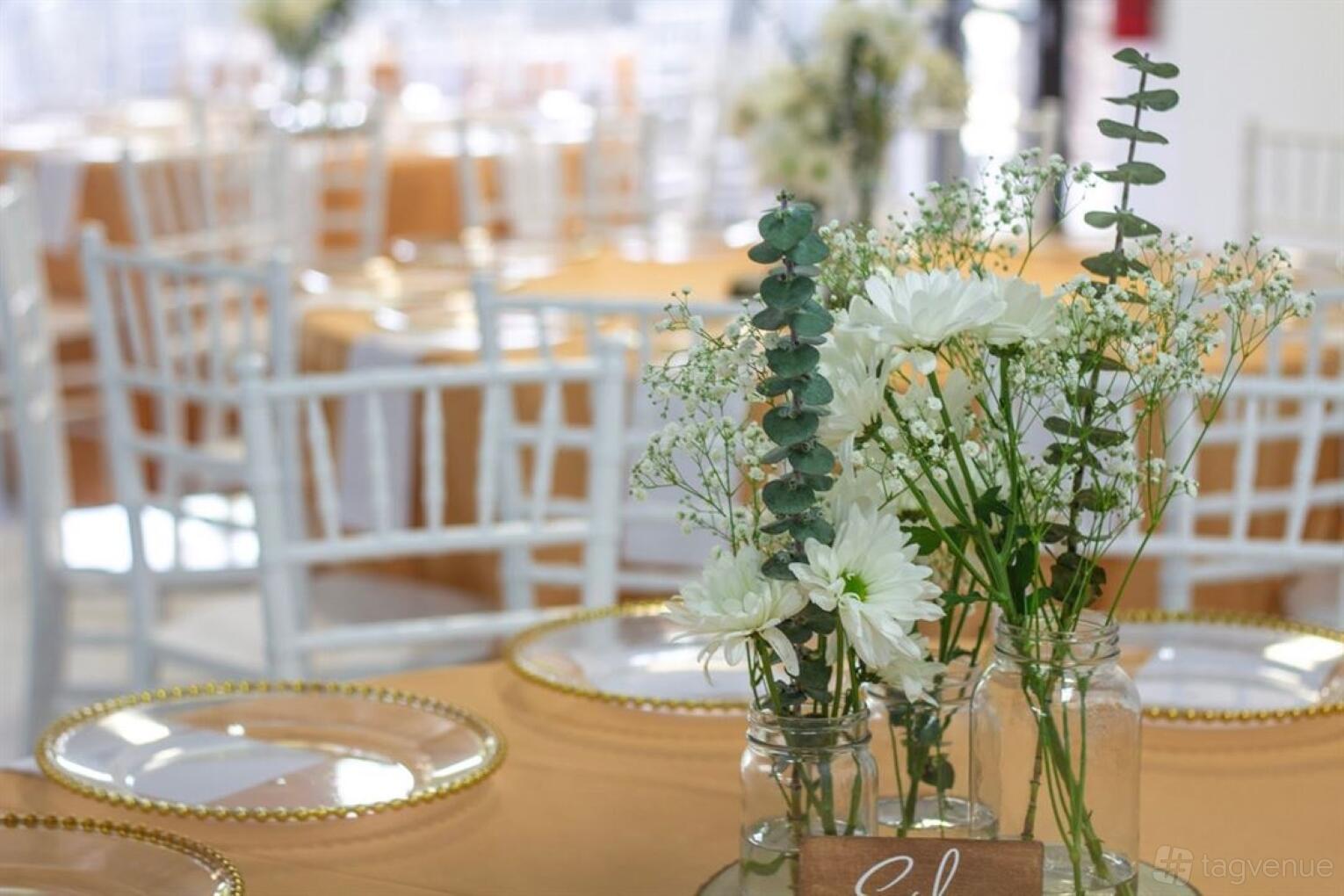 An event venue with round tables draped in gold linens, white chairs, and floral centerpieces at Cachet Events Luxury Venue - Kennesaw.