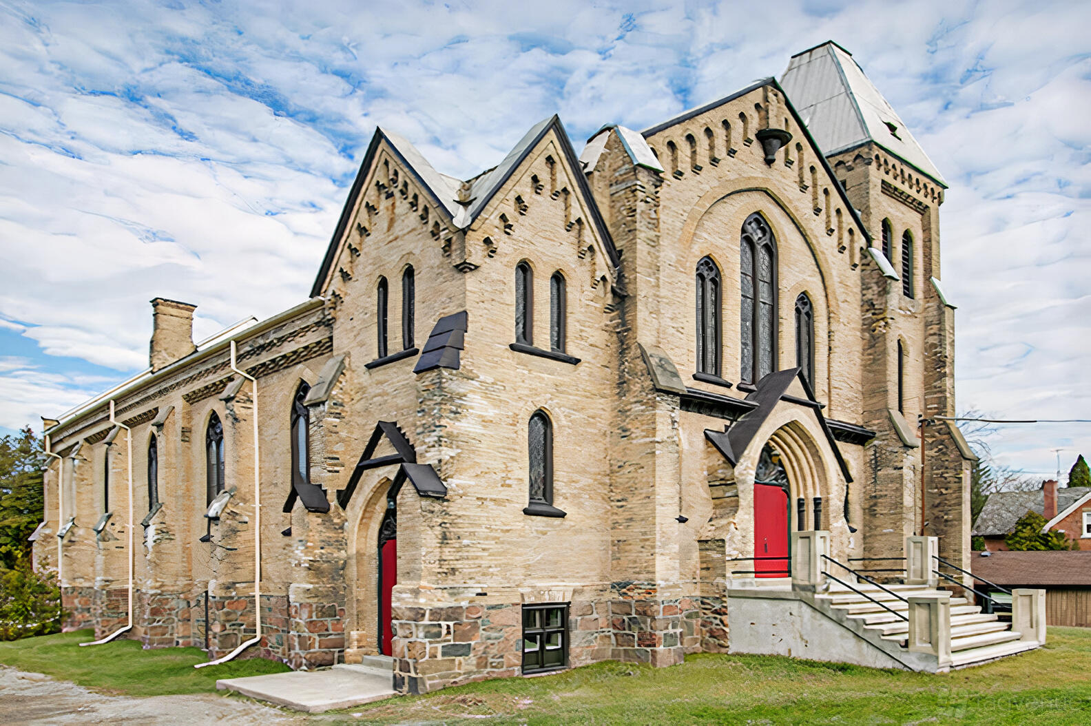 A historic church with pointed arch windows, stone foundations, and red double doors at Millbrook Cathedral.