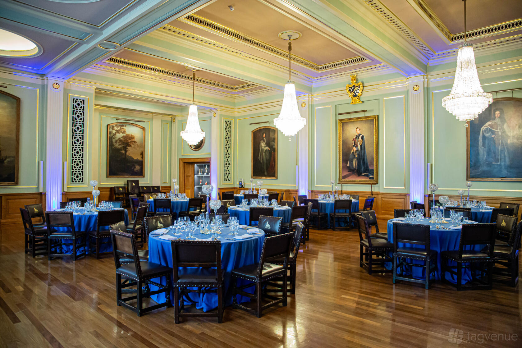 A grand hall with crystal chandeliers, polished wood floors, and round tables with blue linens at No.9 Little Trinity Lane.