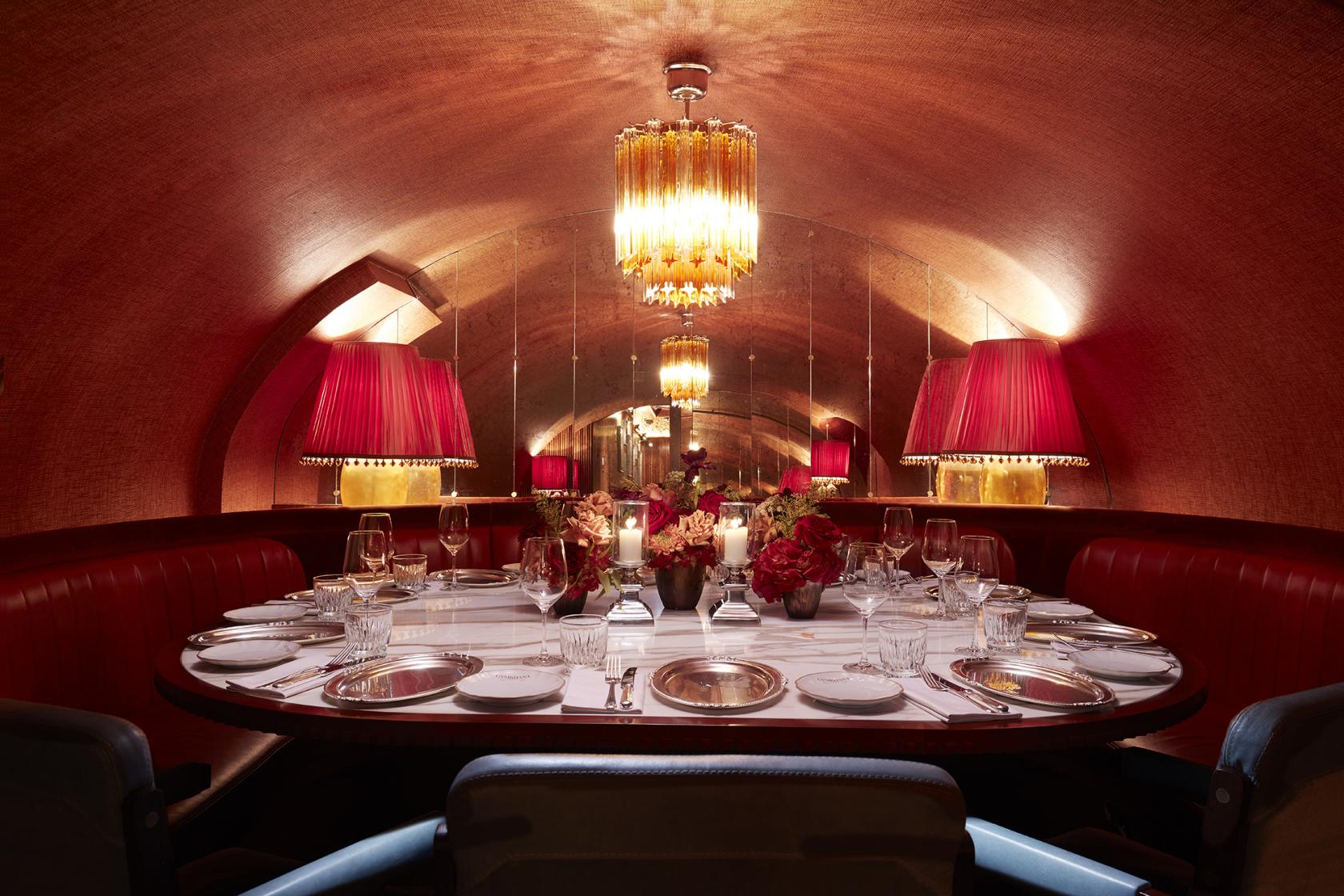 A private dining room with a round table, red leather banquettes, mirrored walls, and chandeliers at Gymkhana.