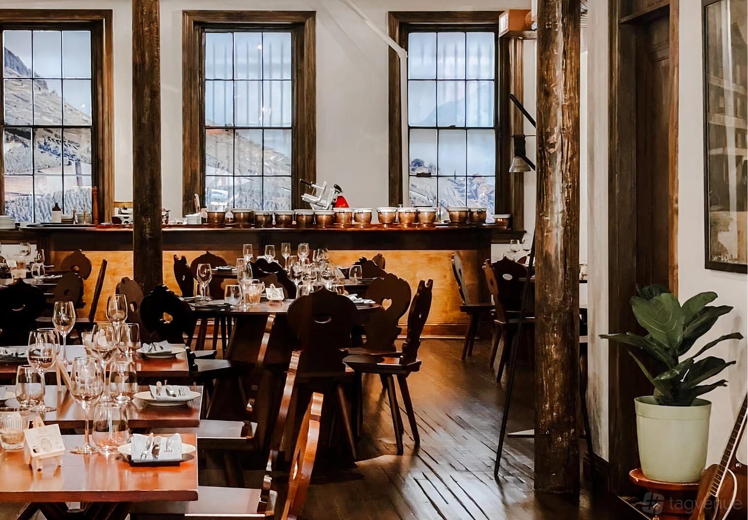A bar with wooden tables, carved chairs, wine glasses, and large windows with mountain views at The Lavaux Wine Bar.