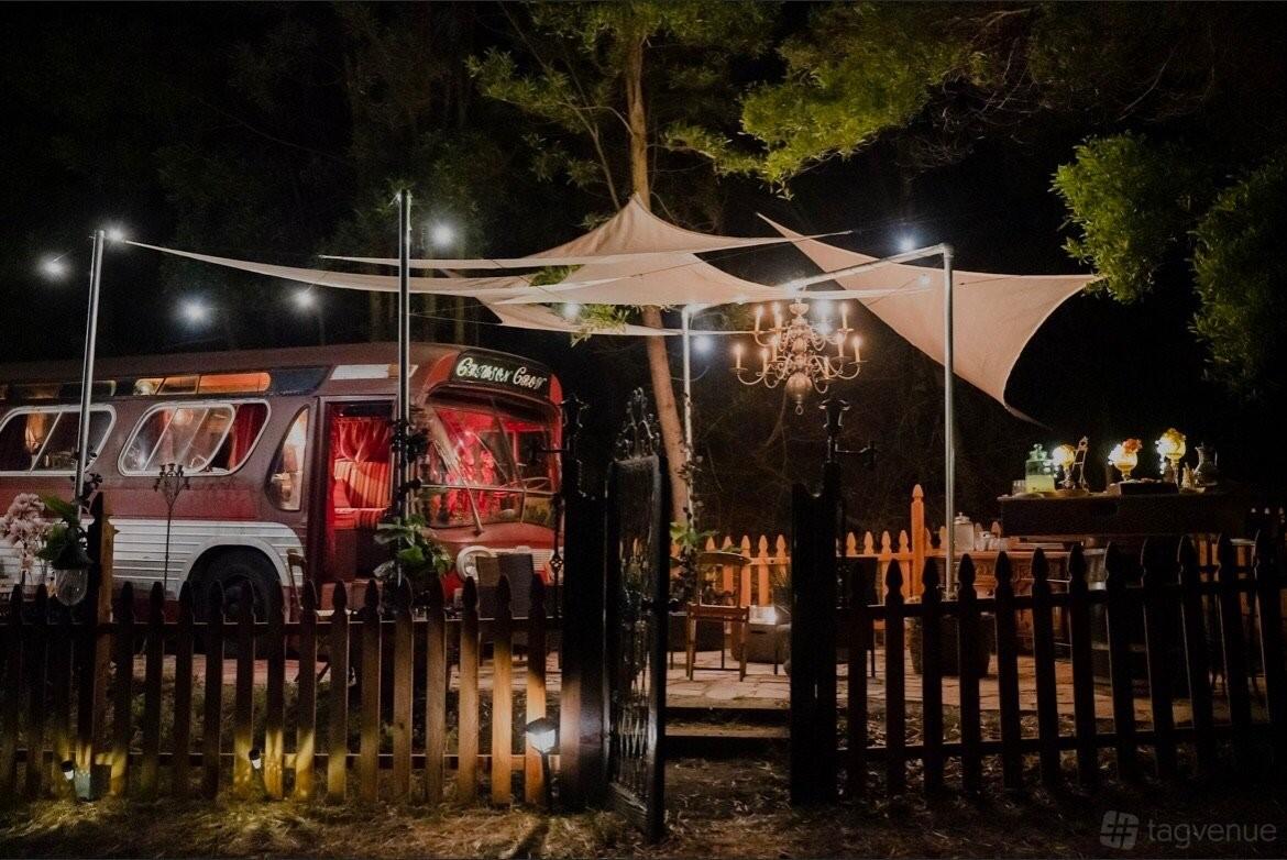 An outdoor event venue with a vintage bus, string lights, chandeliers, and sail canopies at Point San Pablo Harbor.