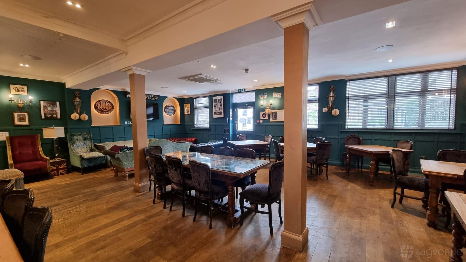 A function room in a pub with wooden floors, mismatched vintage chairs, and framed music memorabilia at Clissold Arms.