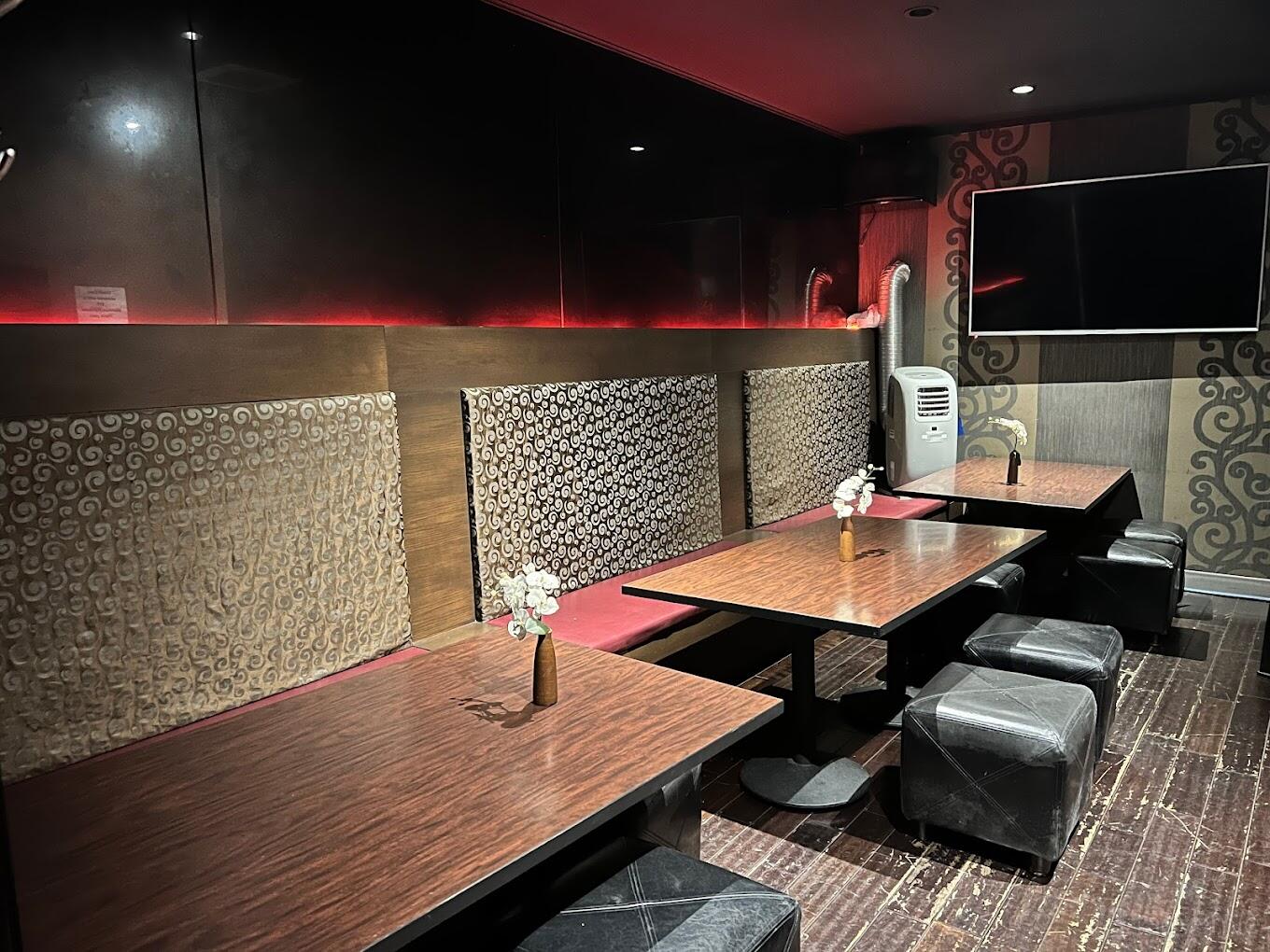 A restaurant private room with wood tables, cushioned bench seating, small floral vases, and wall decor at Harajuku Sushi.