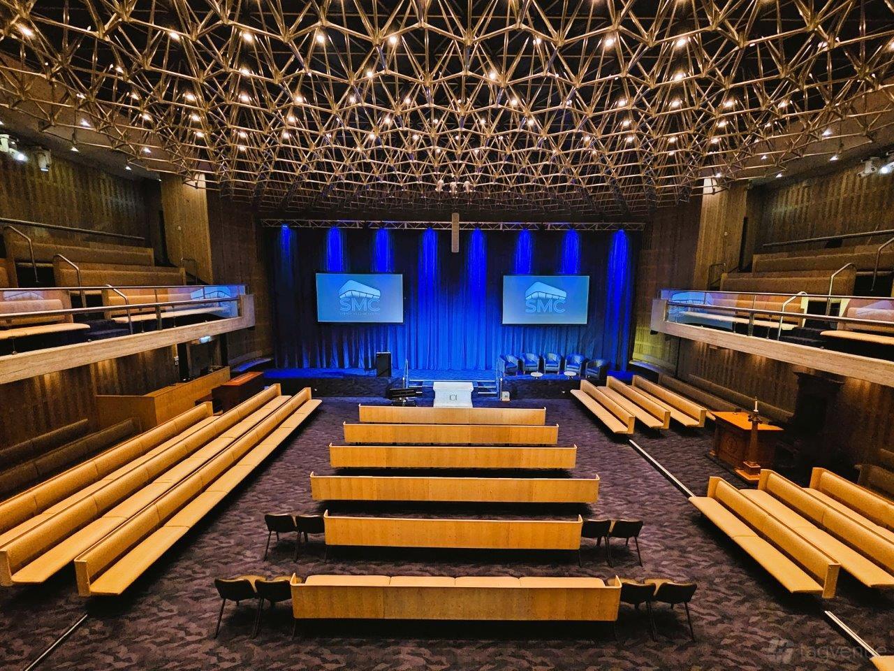 A conference centre with tiered seating, dual projection screens, and geometric ceiling design at Sydney Masonic Centre.