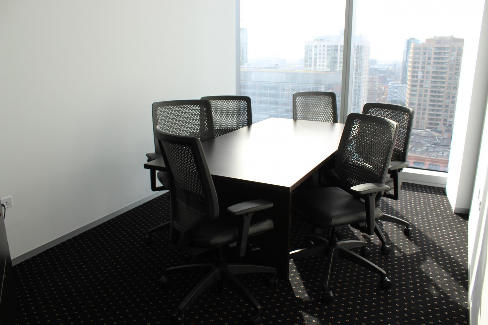 A meeting room with a rectangular table, six mesh office chairs, and floor-to-ceiling windows at Servcorp - River Point.