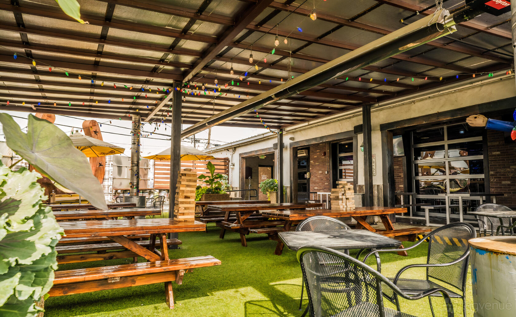 An outdoor space with picnic tables, artificial grass, and string lights at Longhorn Icehouse.