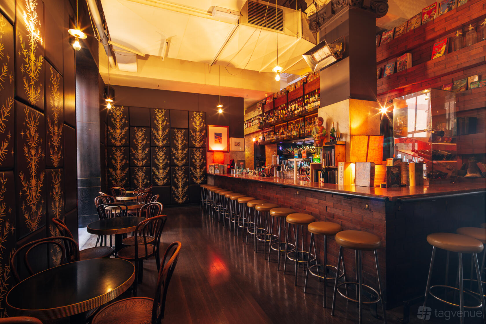 A cocktail bar with a long bar counter, wooden stools, round tables, and tall patterned panels at Cookie.