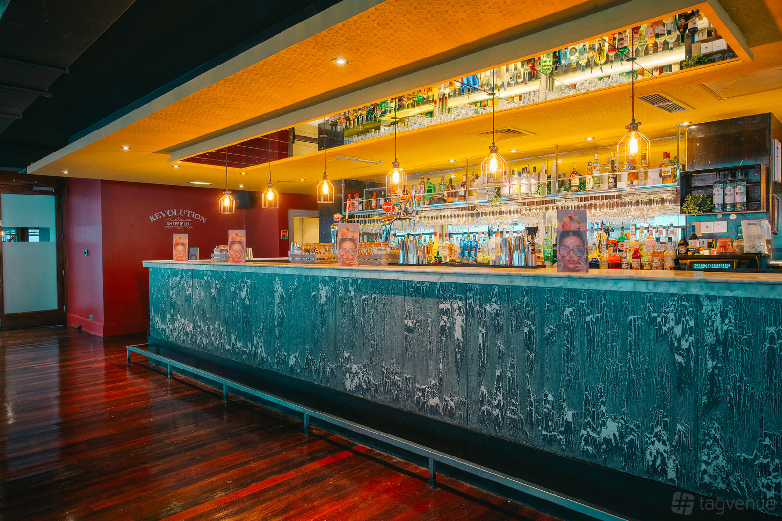 A bar with pendant lighting, extensive backlit shelves of spirits, and a textured blue counter at Revolution Sheffield.