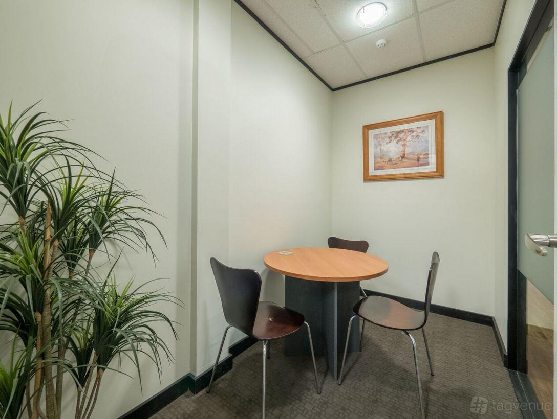 A coworking space with a small round meeting table, two chairs, and a potted plant at M1 Business Centre.