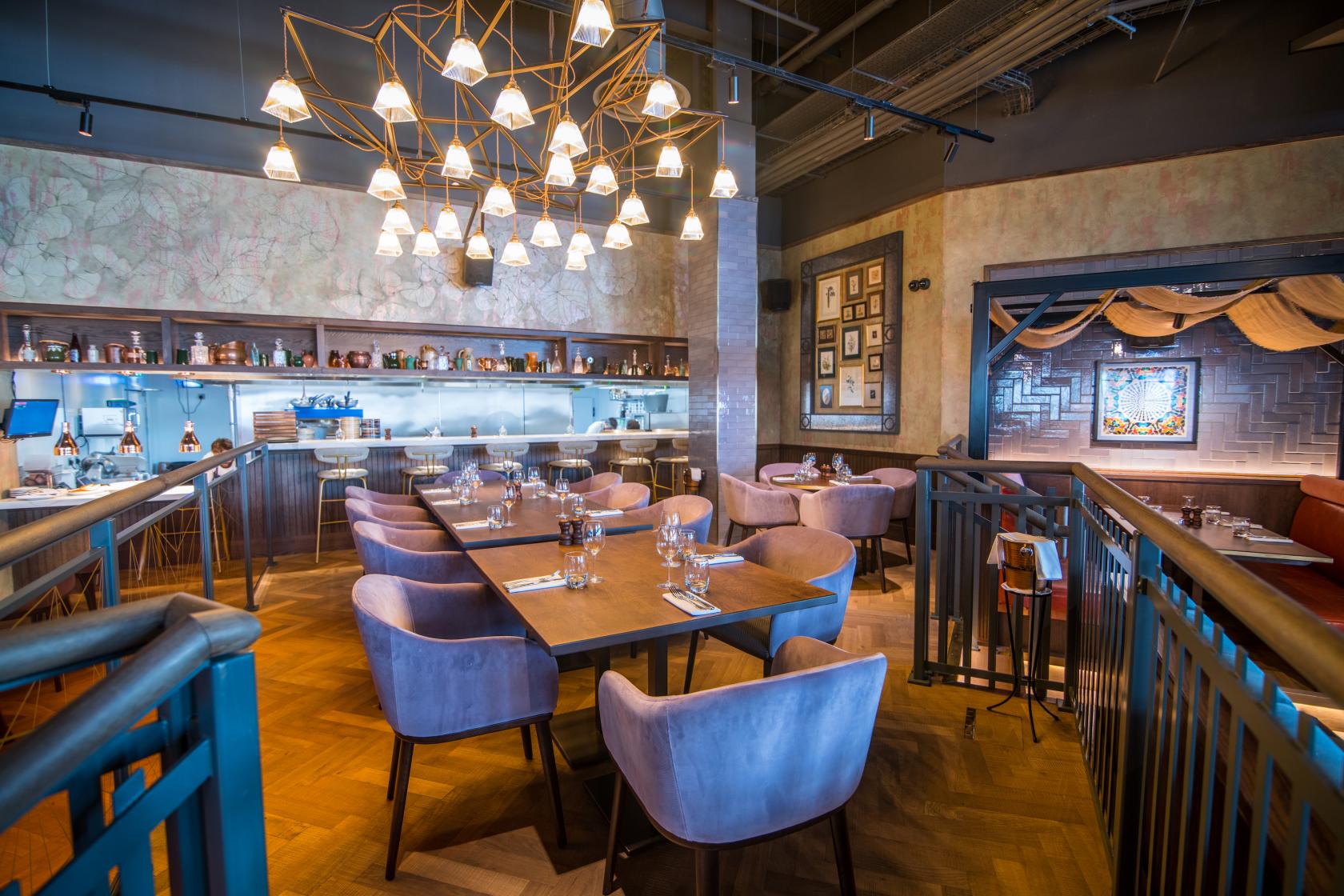 A lounge in a bar with velvet armchairs, a geometric chandelier, and a backlit bar at Westwood.