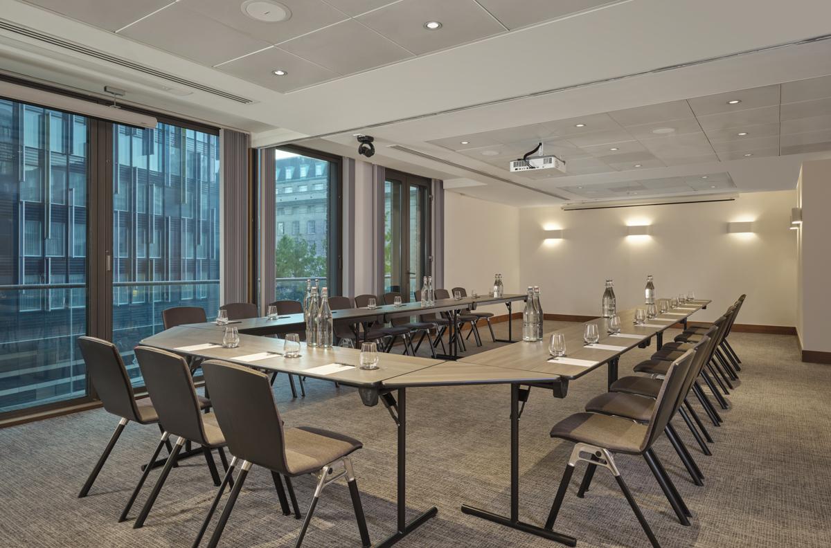 An event space with large windows, U-shaped tables, and a ceiling projector at Park Plaza County Hall London.
