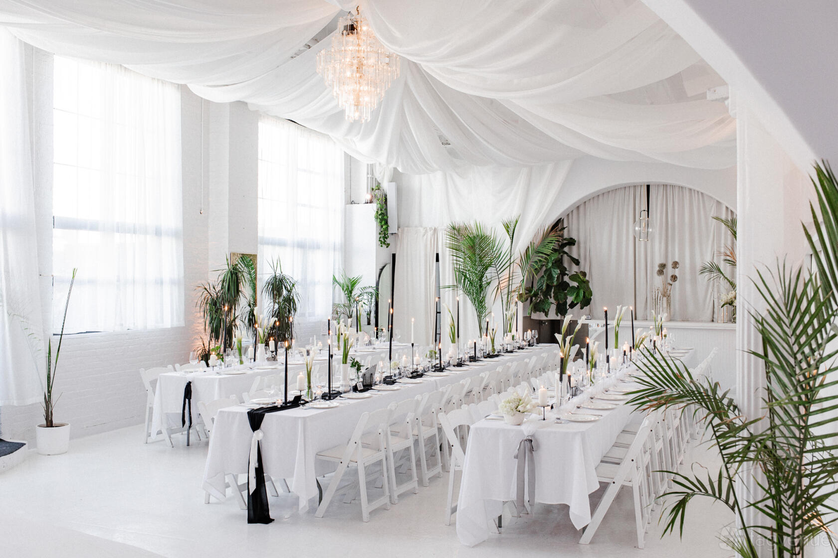An event venue with white draped ceilings, long banquet tables with white linens, and large windows at Atmosfera.
