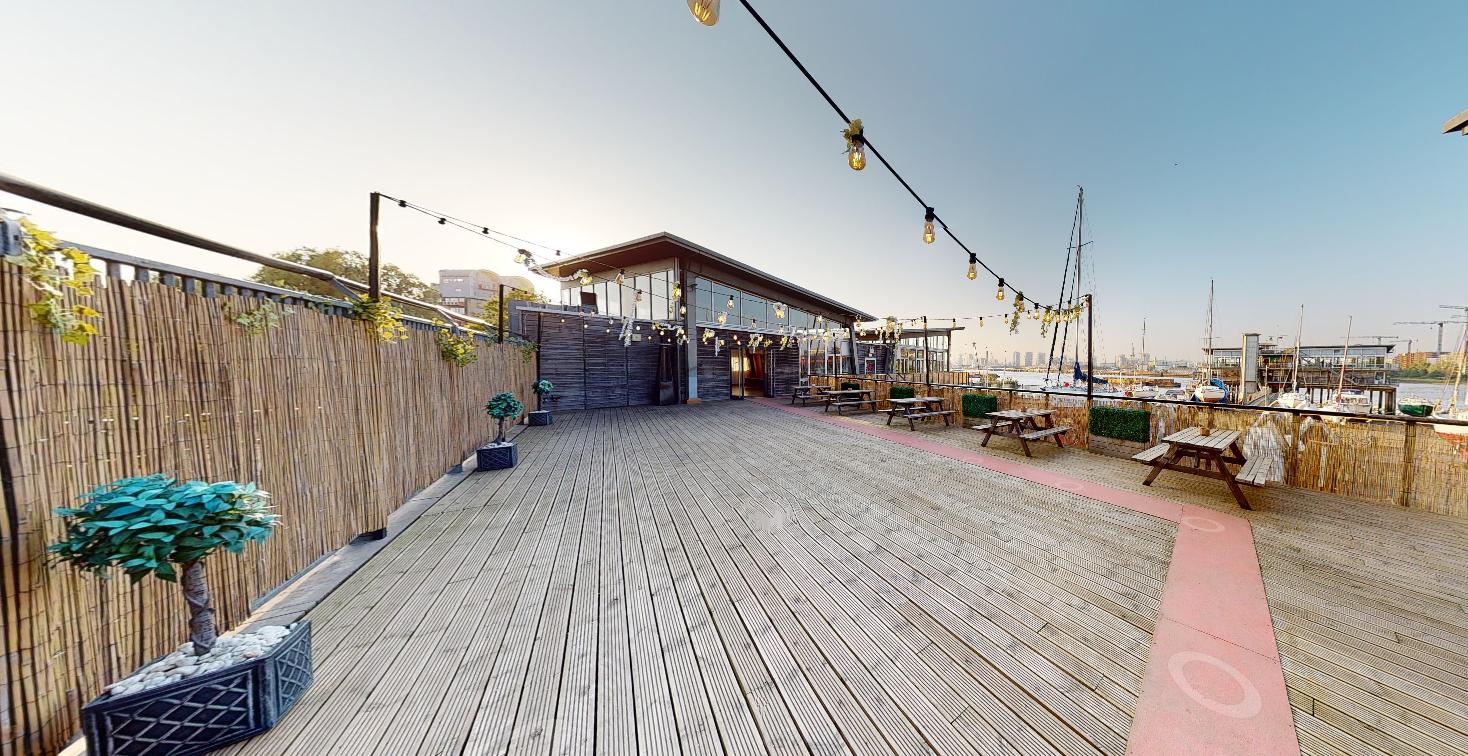 An outdoor event venue with wooden decking, string lights, and picnic tables at Greenwich Yacht Club.